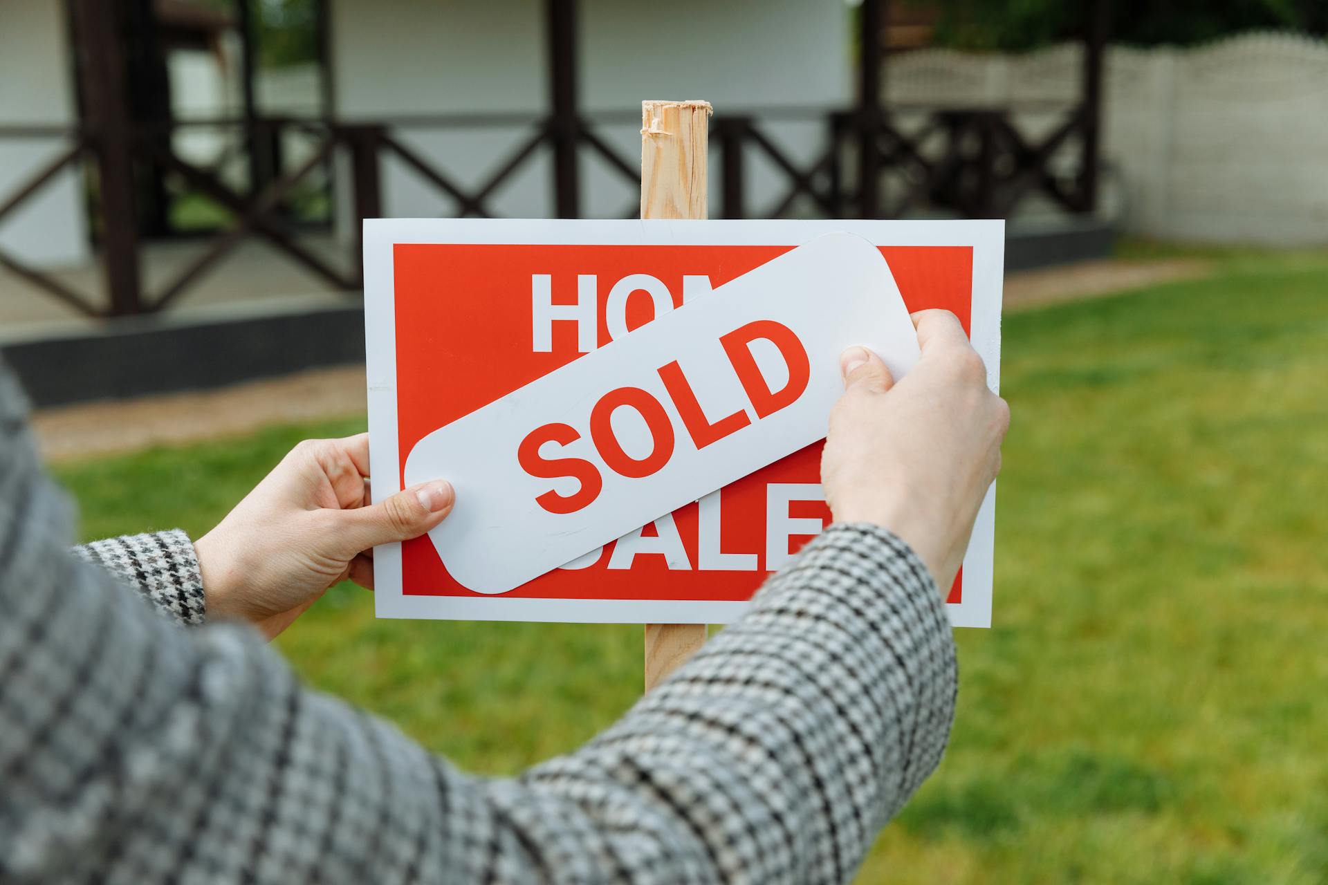 Person placing 'SOLD' sign on house for sale.